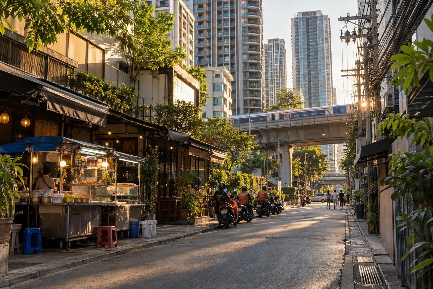 A side soi off Sukhumvit Road in the late afternoon, with condominium towers rising behind low shophouses and the elevated BTS line crossing the end of the street