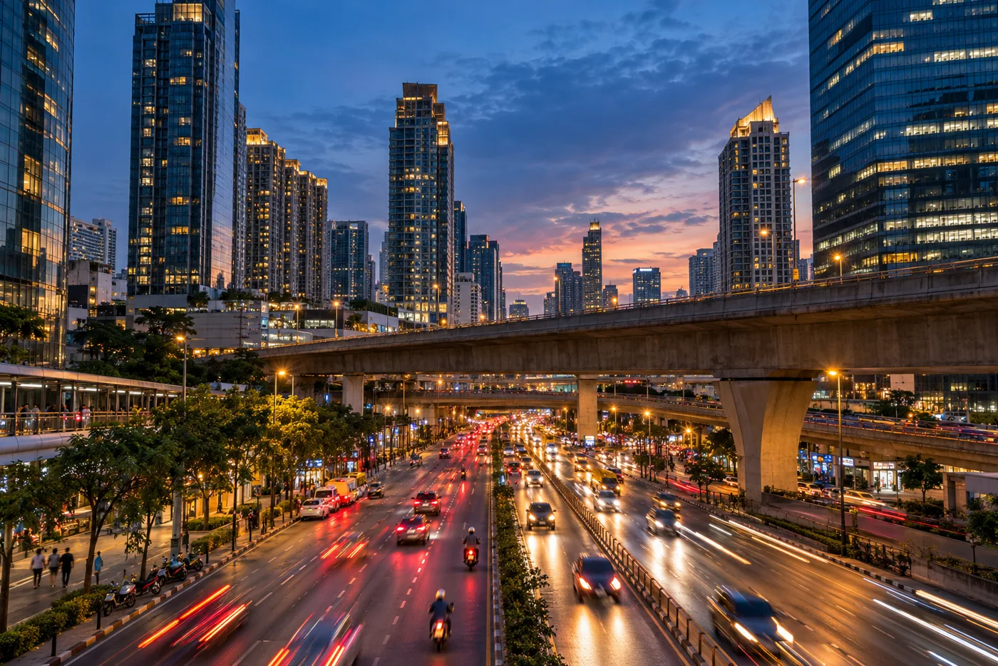 Dusk at the Rama 9 junction in Bangkok, with glass office and residential towers lit up above a wide road, an elevated expressway crossing the scene and traffic light trails below.