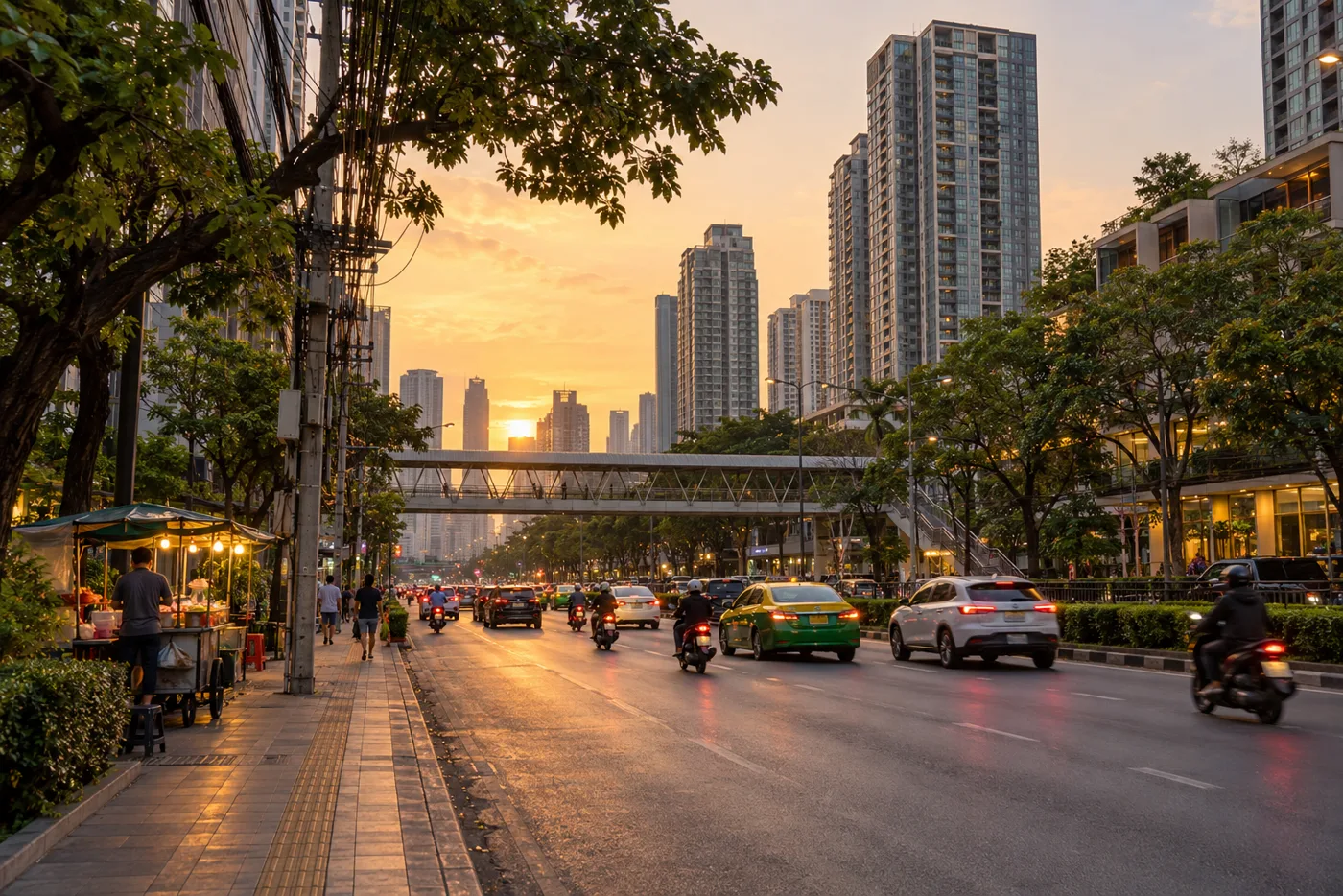 A wide stretch of Rama IV Road in eastern Bangkok in early-evening light, with residential towers beside the road, a pedestrian footbridge and motorbikes in the traffic