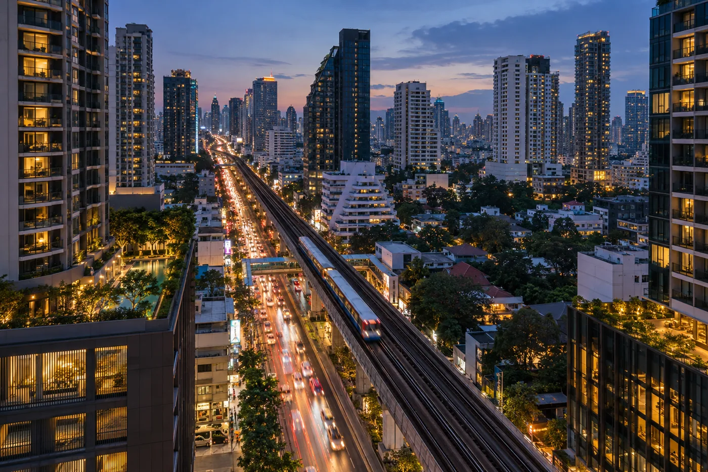 Sukhumvit Road in Bangkok at dusk seen from above, the elevated Skytrain track running between lit condominium towers