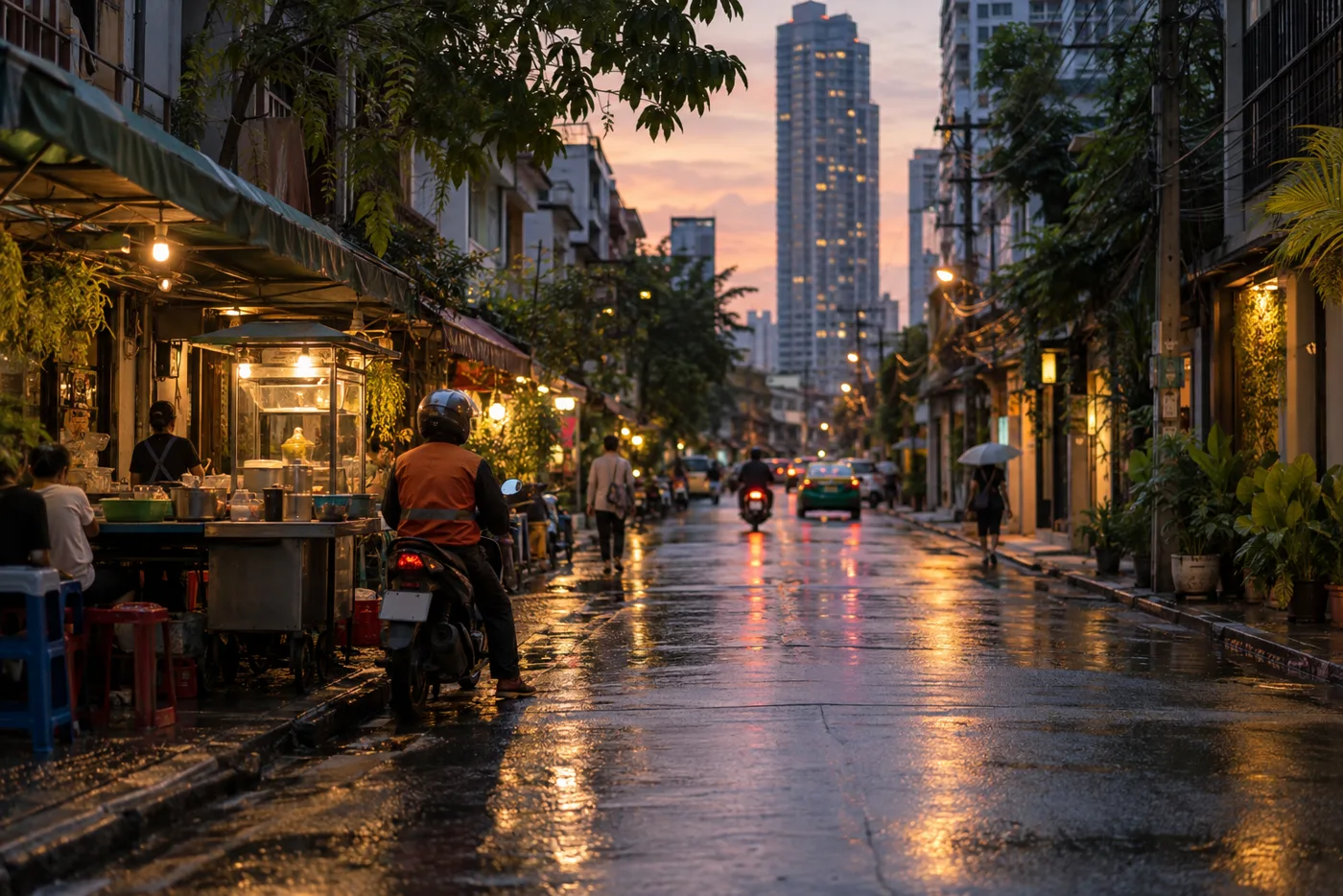 A residential Bangkok side street in early evening, with low shophouses and a food cart on one side and a glass condominium tower behind them.